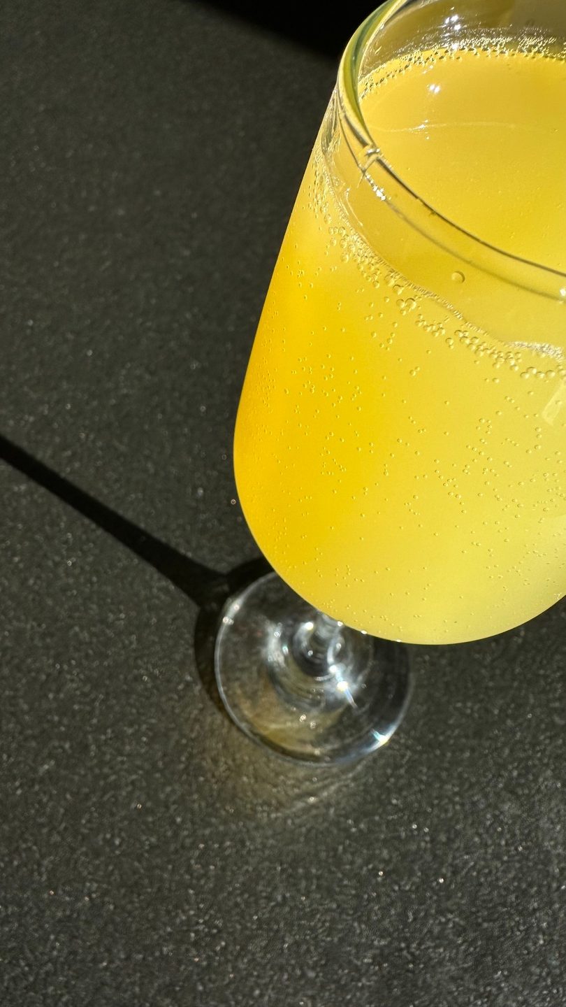 Close-up of a mimosa in a champagne flute, with bubbles and a dark background.