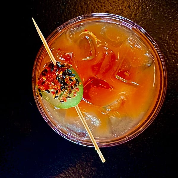 Overhead view of a vibrant orange cocktail with ice, garnished with a spiced cucumber slice.