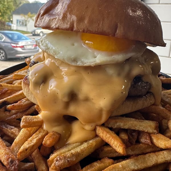 A burger with melted cheese and a fried egg, served on a bed of golden fries.