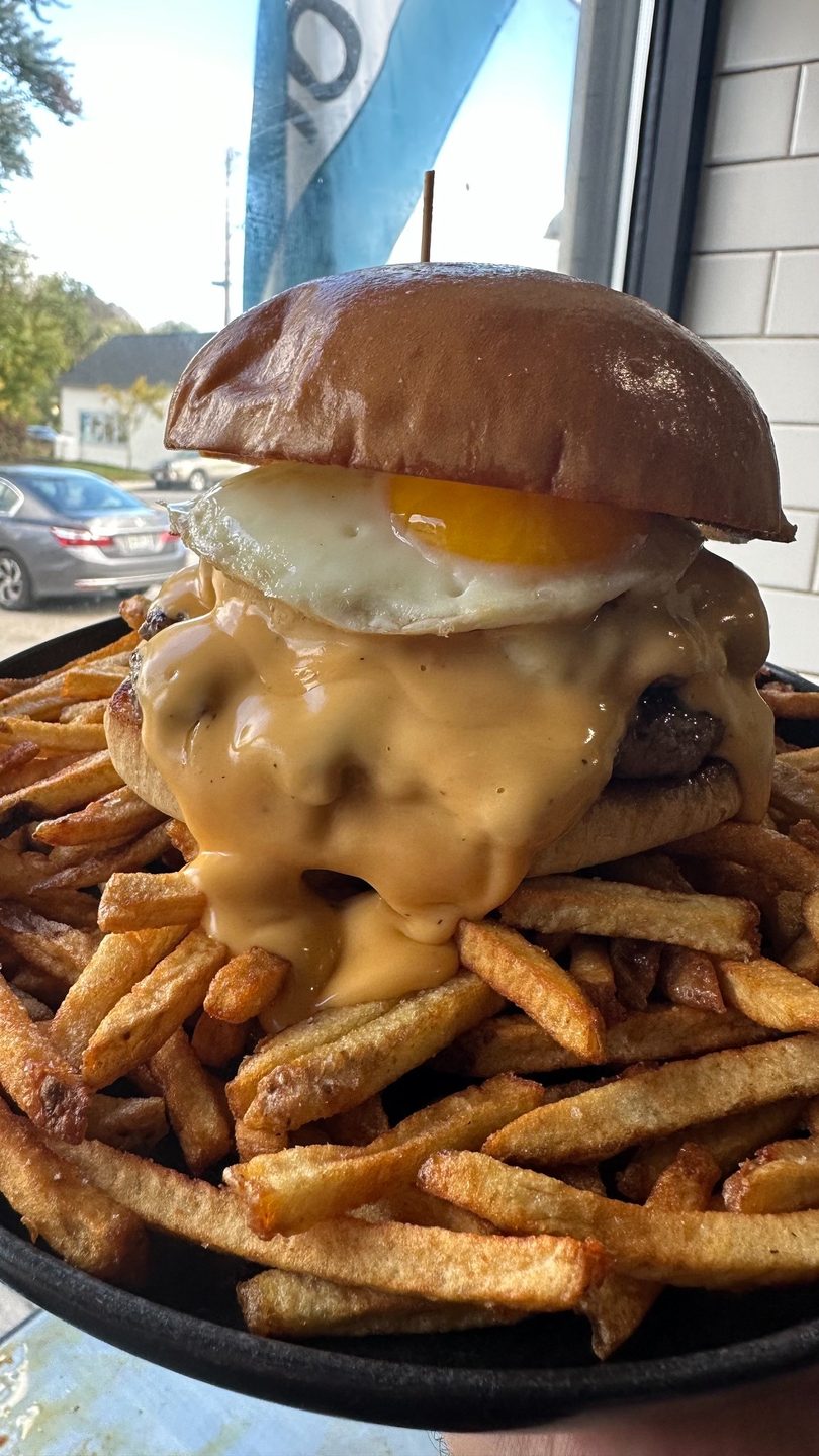 A burger with melted cheese and a fried egg, served on a bed of golden fries.