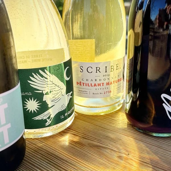 A close-up of five bottles of natural wine, including Pet Nat, Scribe, and Nouveau.