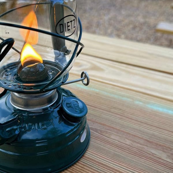 A lit green Dietz lantern sits on a wooden picnic table, providing warm light.