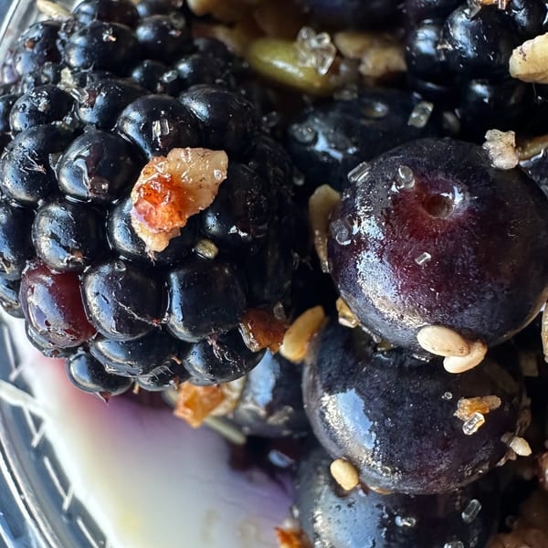 Close-up of fresh blueberries and blackberries with granola and sugar crystals in a clear cup.