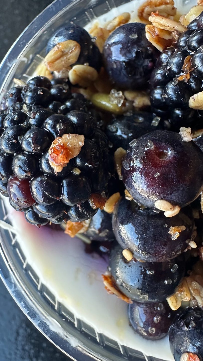 Close-up of fresh blueberries and blackberries with granola and sugar crystals in a clear cup.