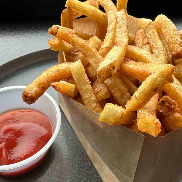 Crispy golden french fries in a paper container with a side of ketchup on a dark plate.