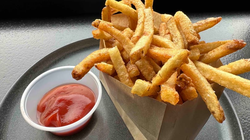 Crispy golden french fries in a paper container with a side of ketchup on a dark plate.