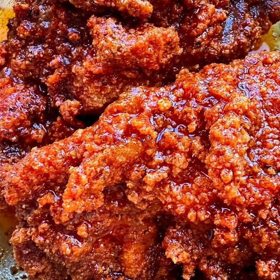 Close-up of crispy, golden-brown fried chicken pieces glistening with a sweet and spicy glaze.
