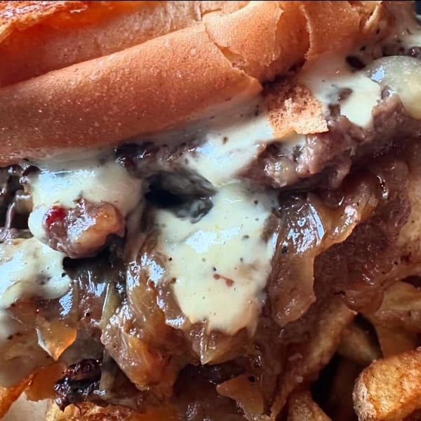 A close-up of a cheesesteak sandwich with melted cheese and caramelized onions, served with fries.