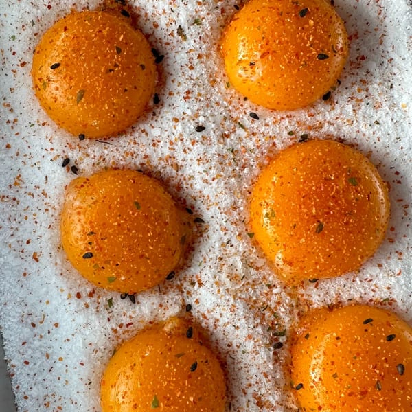 Eight bright orange egg yolks seasoned with spices and black sesame seeds on a bed of salt.