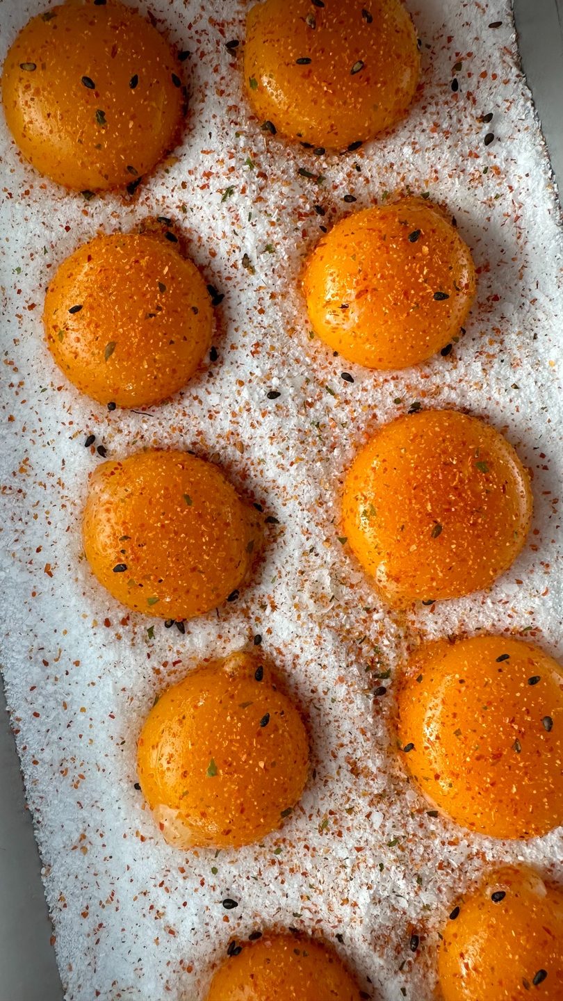 Eight bright orange egg yolks seasoned with spices and black sesame seeds on a bed of salt.