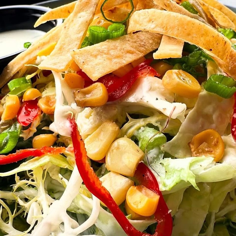 Close-up of a vibrant salad with lettuce, corn, red peppers, tortilla strips, and dressing.