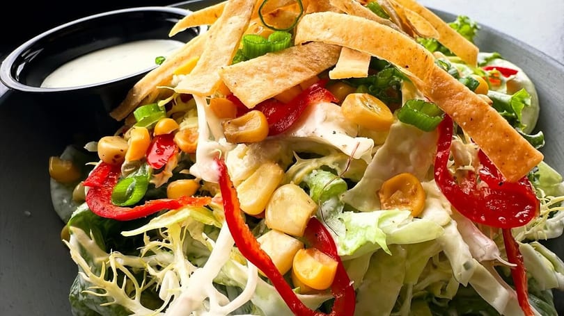 Close-up of a vibrant salad with lettuce, corn, red peppers, tortilla strips, and dressing.