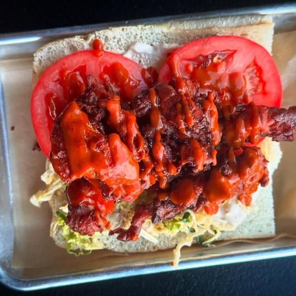 Spicy fried chicken sandwich with tomatoes, lettuce, and sauce on a metal tray.