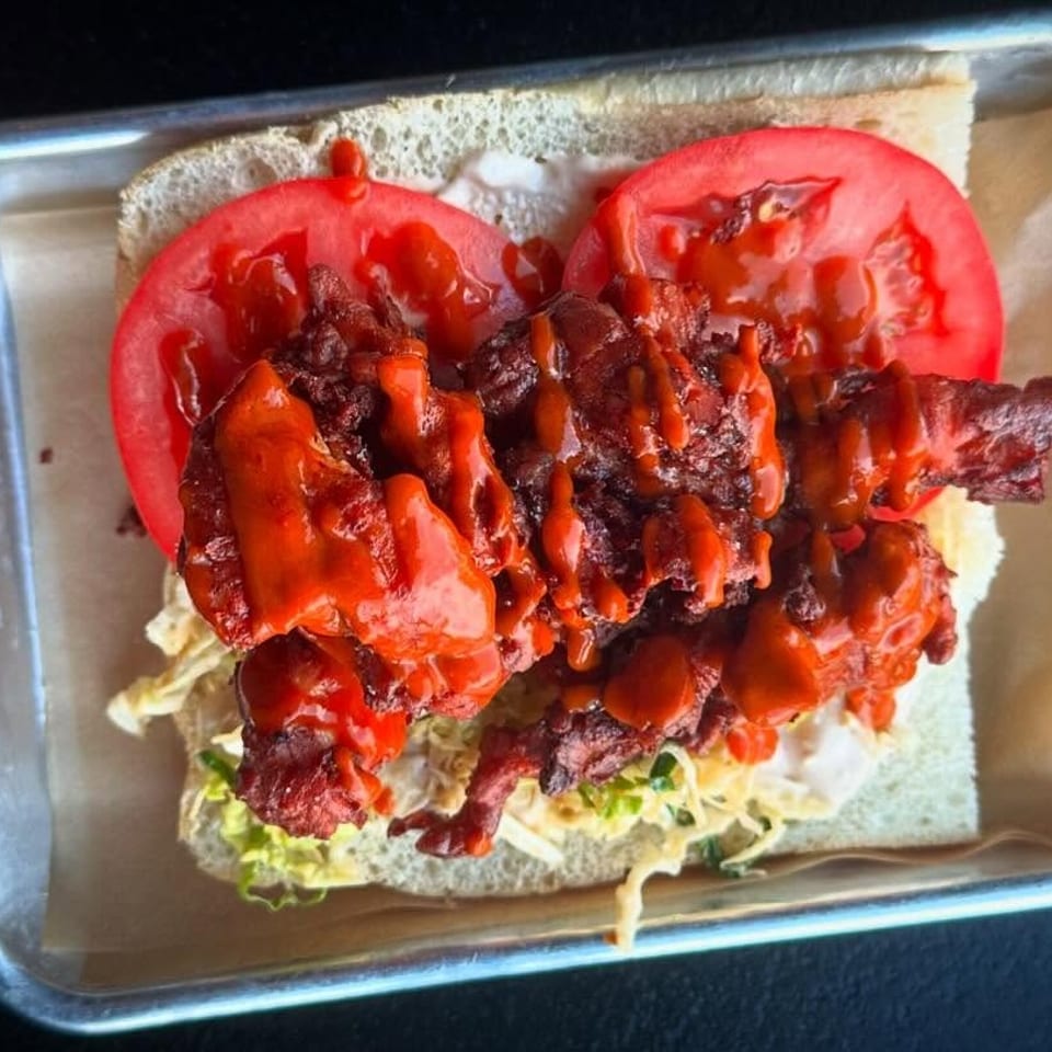 Spicy fried chicken sandwich with tomatoes, lettuce, and sauce on a metal tray.