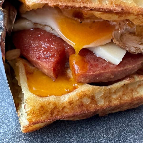 Close-up of a breakfast sandwich with sausage, egg, and cheese on toasted bread, wrapped in foil.