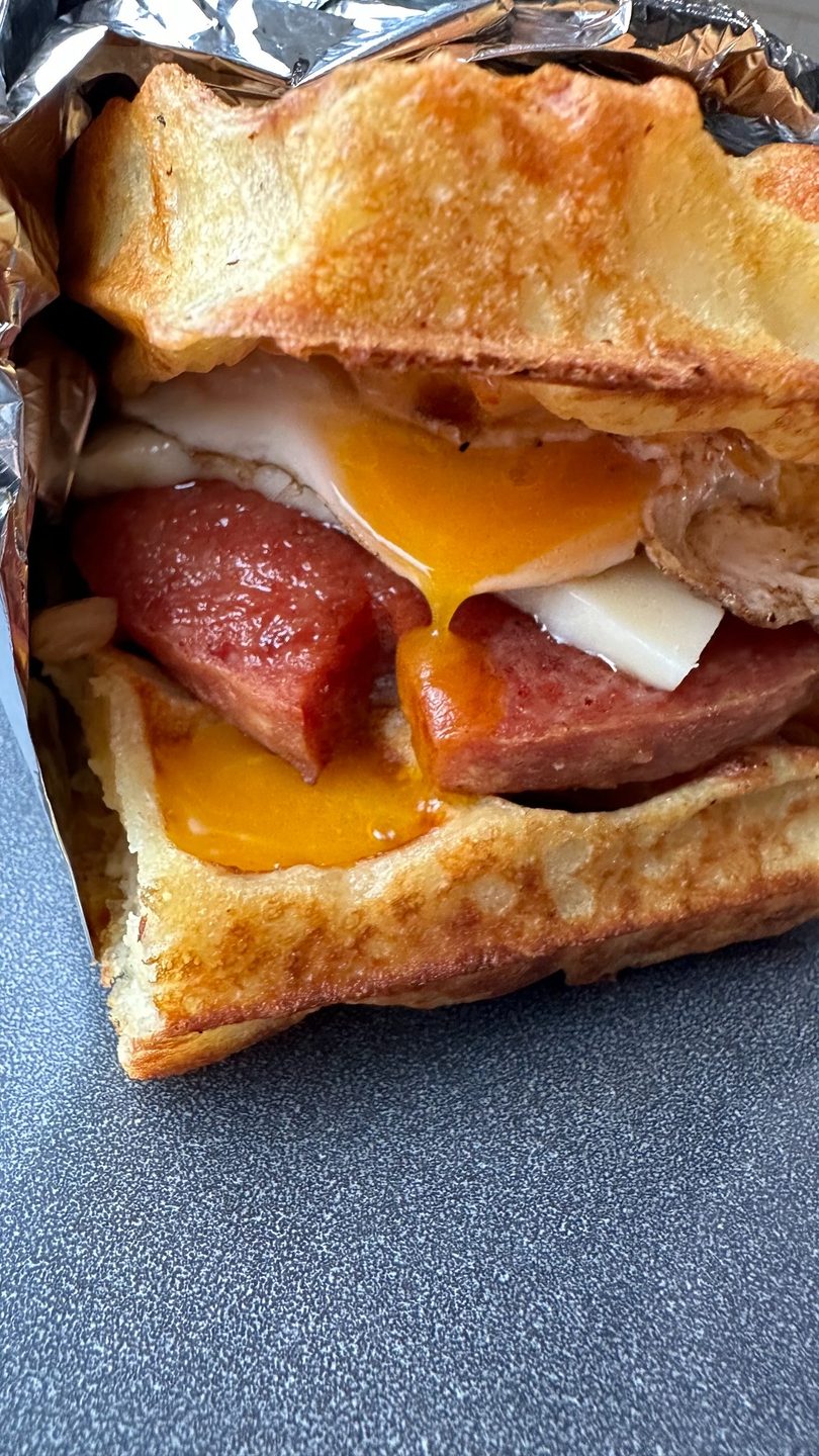 Close-up of a breakfast sandwich with sausage, egg, and cheese on toasted bread, wrapped in foil.